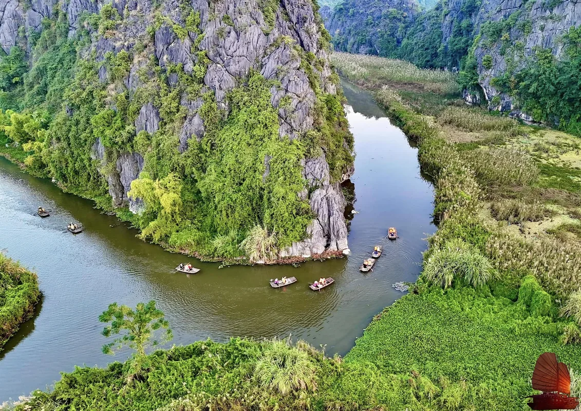 A quiet wooden rowboat floating along the glassy river through the limestone caverns of Trang An.